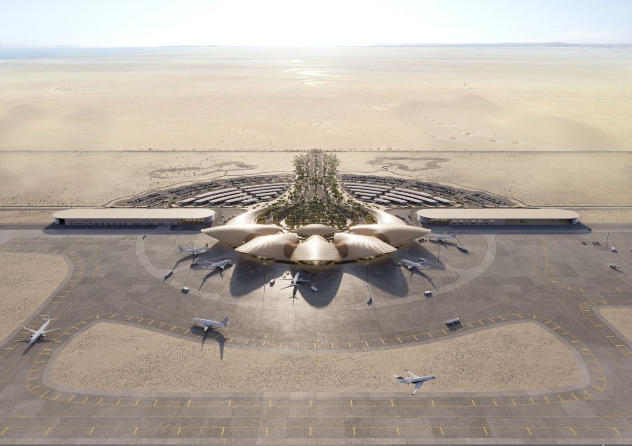 An aerial view of a futuristic airport in a desert landscape, featuring a lotus-shaped terminal building with a lush green central core.
